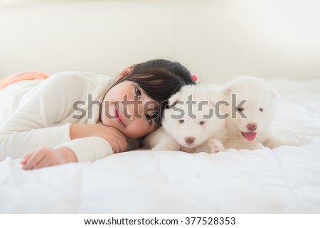 Little asian girl lying with two siberian husky puppies on bed
