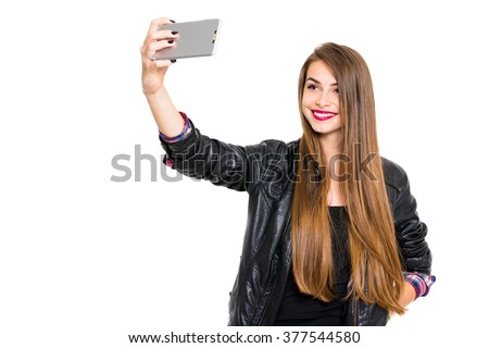 Cool blonde teenage girl in black leather jacket smiling, taking a selfie on smartphone. Beautiful young woman photographing herself using cellphone. Horizontal, isolated on white, copy space.