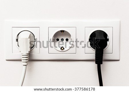 Triple electrical socket on white wall with two plugged cables
