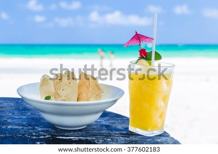 Fresh cold tasty alcohol cocktail with orange juice, tequila, lime, ice and mexican nachos with guacamole sauce close-up with people on background at tropical exotic sandy beach in the Caribbean sea