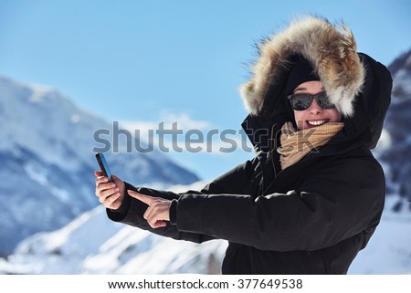 Young happy woman with mobile phone with mountains in background trying to establish communication or taking pictures or selfie with her cell phone