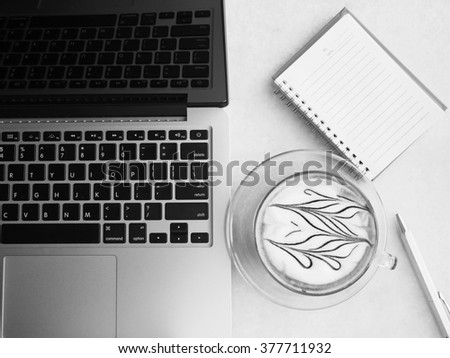 Monochrome cup of coffee with laptop, notebook and pen for work