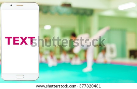 Girl use smart phone, blur image of taekwondo class as background.