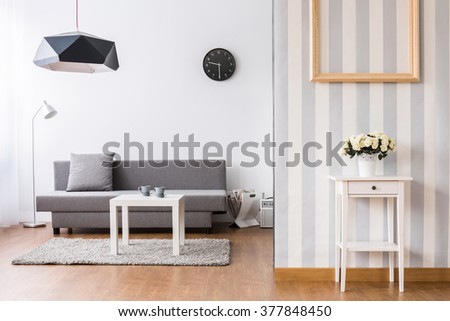 Stylish living room with grey sofa and small coffee table. Light interior with flooring and decorative wallpaper. Royalty-Free Stock Photo #377848450