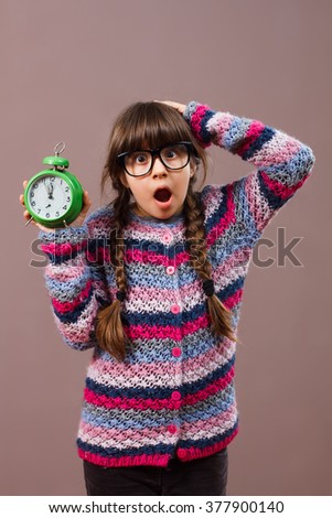 Cute little nerdy girl is in panic because she doesn't have too much time to do something. Little nerdy girl in panic holding clock