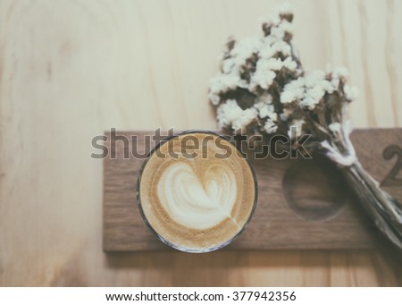 Cup of cappuccino with latte art on a wooden plate and wooded table decorated with dried flower, Selective focus ,Vintage tone