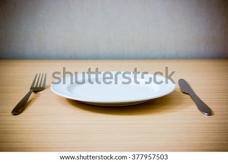 Empty plate with fork and knife on wooden table. Table arrangement. Vintage effect style picture