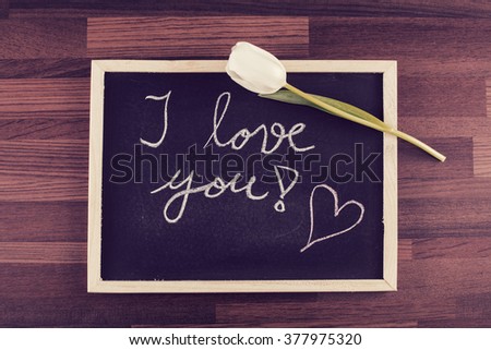 White rose and a blackboard with written text: "I love you!" Image includes a vintage effect.