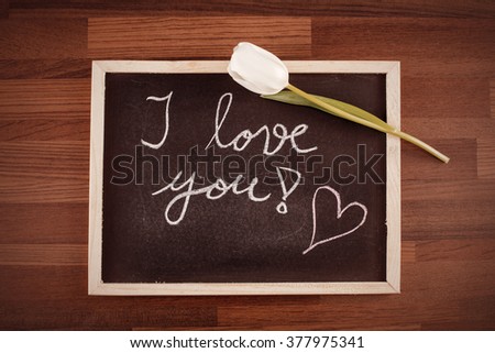 White rose and a blackboard with written text: "I love you!" Image includes a vintage effect.