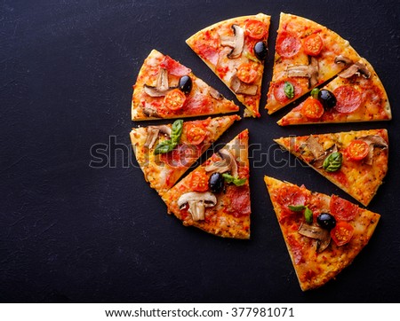 Cut into slices delicious fresh pizza with mushrooms and pepperoni on a dark background. Top view. Copyspace. Pizza on the black table.  Royalty-Free Stock Photo #377981071