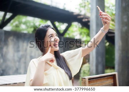 Asian woman taking a selfie with her phone in public park