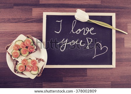 Delicious sandwich, white rose and a blackboard with written text: "I love you!" Image includes a vintage effect.