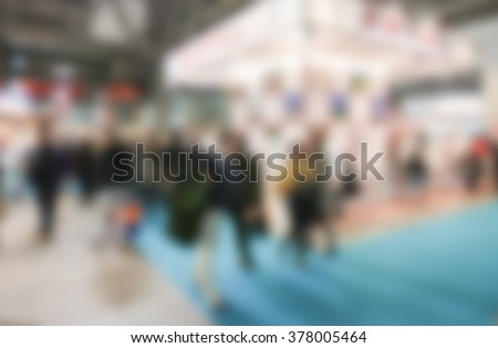 People crowd visit a trade show, humans unrecognizable. Background with an intentional blur effect applied.