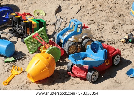 Beautiful plastic childish multicolored yellow red blue green transport childish toys laying in sandbox summer outdoor playtime closeup on sand background, horizontal picture 