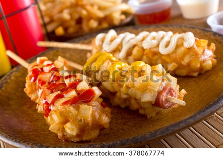 Delicious crunchy korean style chunky corn dogs with batter and fried potatoes. Royalty-Free Stock Photo #378067774