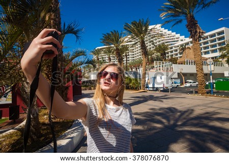 Nice girl making selfie with a camera at the palm promenade of Eilat, Israel