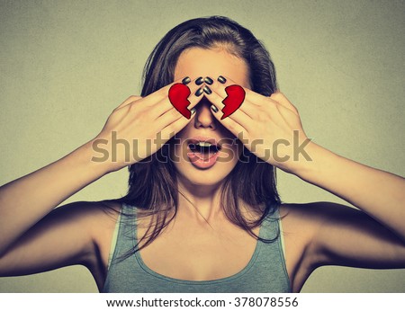 Beautiful young woman eyes covered by hands with broken heart printed on them. Girl in love isolated on gray wall background    Royalty-Free Stock Photo #378078556