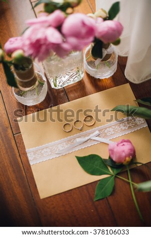 rose peonies with greenery in glass stand on wooden floor with wedding invitation and wedding rings
