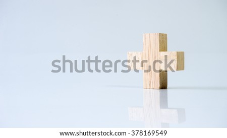 Single block cross wooden letter T or plus sign symbol. Isolated on empty background. Slightly de-focused and close-up shot. Copy space.