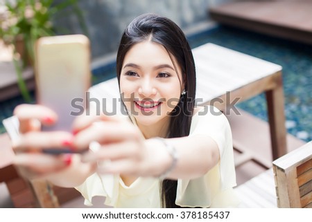 Asian woman taking a selfie with her phone in public park (focus on her face)