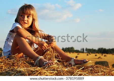 Summer is a little life. Picture of a little girl seating on a stack of hay in a wheat field against the bright blue sky