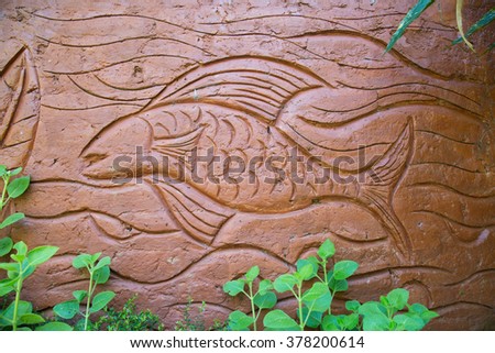 Terracotta art/ Tribal art, picture of a fish in ocean/ sea/ lake/ pond/ water. Carved image in terracotta in a park with lush green plants in  Wayanad,India. Fremont indian culture petroglyph