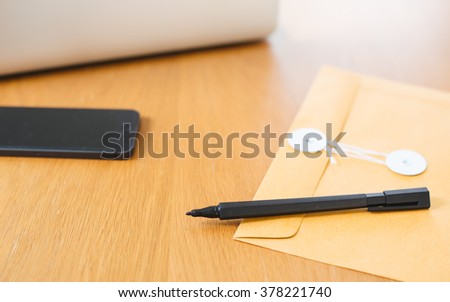 Black pen and brown envelope on wood table with laptop and mobile phone background.