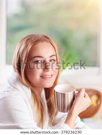 Portrait of cute blond girl drinking morning coffee on the kitchen at home, enjoying breakfast, happy domestic lifestyle