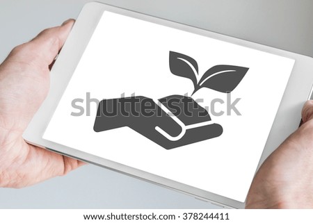 Sustainable concept visualized by hand holding growing plant displayed on touch screen of mobile tablet.
