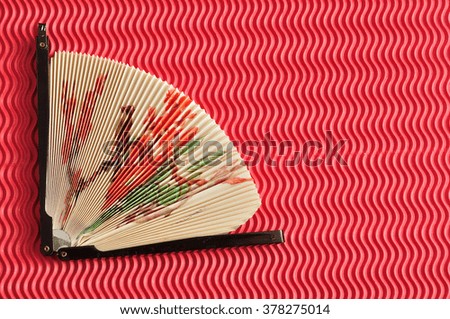 A colorful hand fan decorated with a picture isolated on a red background