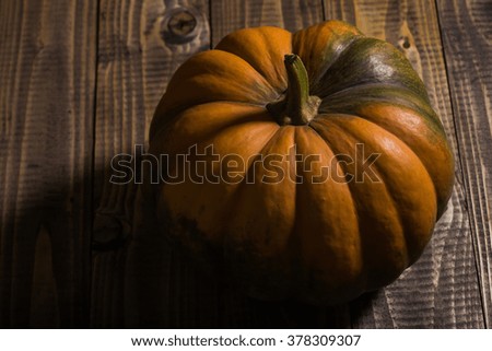 Whole big beautiful ripe flat round orange cucurbita with segmented surface and green formless blotch on brown wooden table, horizontal photo