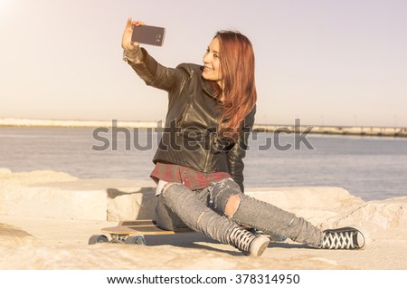 Pretty Caucasian girl is taking a selfie on her skateboard outdoor - concept about sport, people and technology