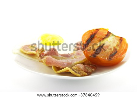 Slices of crispy pork bacon with half a grilled tomato and a fried egg on a white round plate with a white background