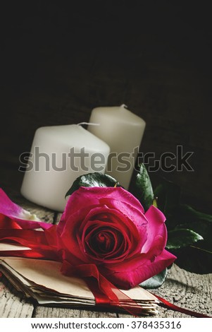 Vintage composition with fresh pink rose, a bundle of old letters, darkened with age, tied with red flight, toned image, selective focus