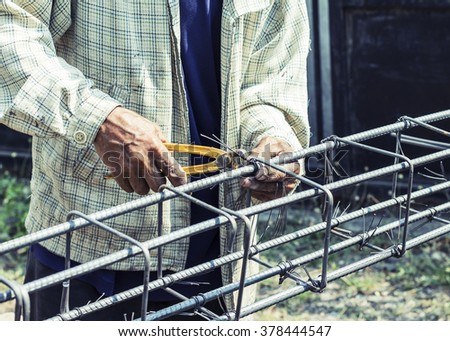 image of workers hands using steel wire and pincers to secure rebar before concrete is poured over it. vintage color