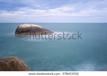 Long exposure seascape with foamy waves splashing against a rocky shore of Samui Island, Thailand