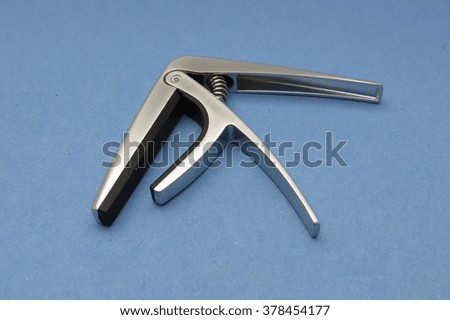 A capo to fit unto the neck of a guitar over light blue background