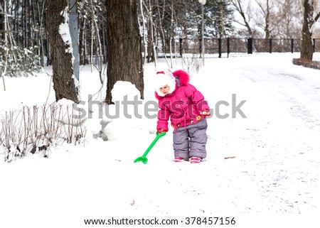 The child, a little girl, obedient daughter playing in the park with a shovel, raaschischaet snow, winter landscape, walk in the park in winter