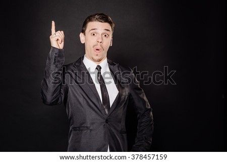 young businessman in black suit pointing his finger up. emotions and people concept. image on a black background.