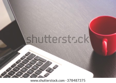 Blurred matte laptop and red coffee cup on a desk