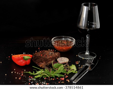 Cooked meat beef steak on the plate with spices, rosemary and garlic and glass of red wine on black background, copy space