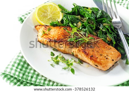 grilled salmon with thyme, lemon and spinach on a plate, vegetarian low carb dish, green napkin on a white background, selected focus, narrow depth of field Royalty-Free Stock Photo #378526132