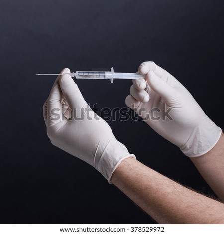 Male hands in latex gloves holding a syringe on dark background