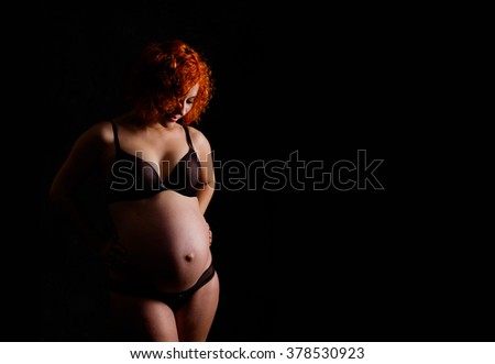 Pregnant woman looking on her belly isolated on black background with copy space for text. Pregnant woman with hands over tummy. Family, love and care wallpaper. 