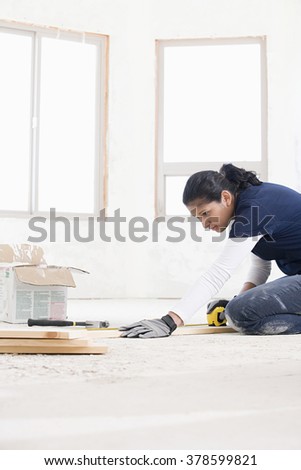A female builder measuring a plank of wood
