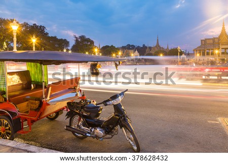 A Tuk Tuk is parked in front of Phnom Penh Royal Palace in Cambodia capital city. The traffic is captured with long exposure to give contrast with the immobile vehicle.