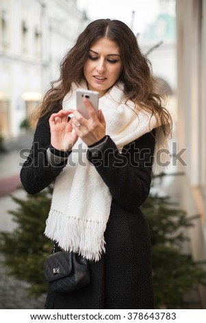 portreit of attractive young girl with long curly hair holding a mobile phone on the background of urban buildings.