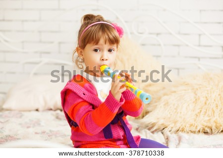 girl in bright cardigan sitting on a bed and playing a trumpet