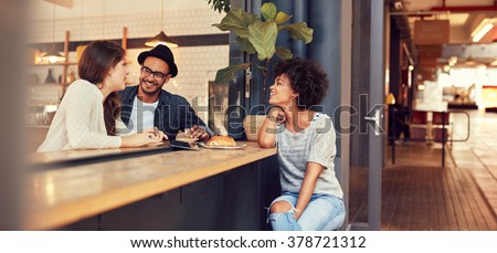 Portrait of three young people sitting together at a cafe. Group of young friends meeting in a coffee shop. Royalty-Free Stock Photo #378721312