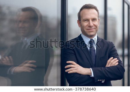 Single confident and handsome male businessman in blue suit and necktie with grin leaning on window outdoors Royalty-Free Stock Photo #378738640